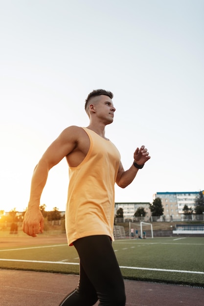 Bel giovane atleta sportivo in abbigliamento sportivo che corre all'aperto al tramonto Ragazzo forte allenamento e jogging nello stadio