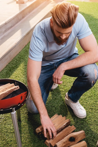 Bel giovane barbuto guardando legna da ardere per grill all'aperto