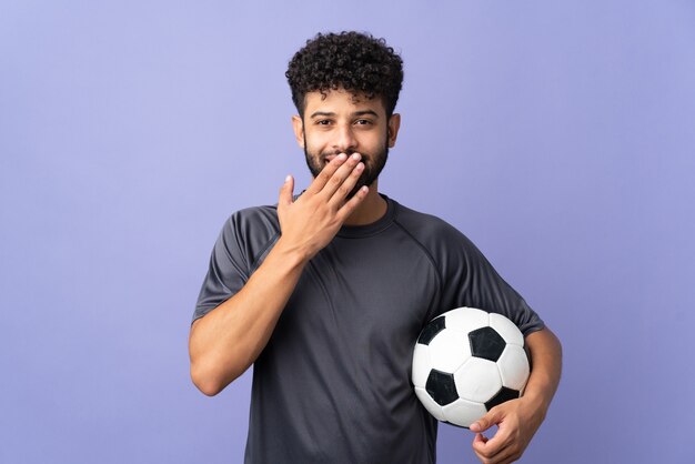 Bel giovane calciatore marocchino uomo sopra isolato su viola felice e sorridente che copre la bocca con la mano