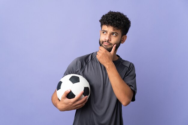 Bel giovane calciatore marocchino uomo sopra isolato sul muro viola e alzando lo sguardo