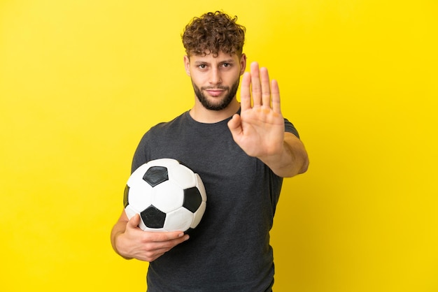 Bel giovane calciatore uomo isolato su sfondo giallo che fa il gesto di arresto