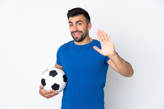 Bel giovane calciatore uomo sopra la parete isolata che saluta con la mano con l'espressione felice