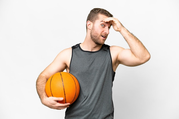 Bel giovane che gioca a basket su sfondo bianco isolato facendo un gesto a sorpresa mentre guarda di lato