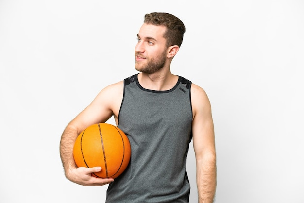 Bel giovane che gioca a basket su sfondo bianco isolato guardando al lato e sorridente