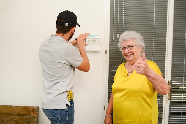 Bel giovane che installa una telecamera antifurto per la sicurezza domestica e un allarme sirena in una casa di una donna anziana