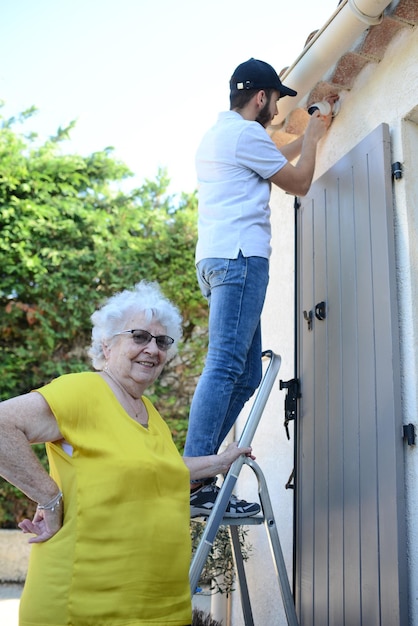 Bel giovane che installa una telecamera antifurto per la sicurezza domestica e un allarme sirena in una casa di una donna anziana