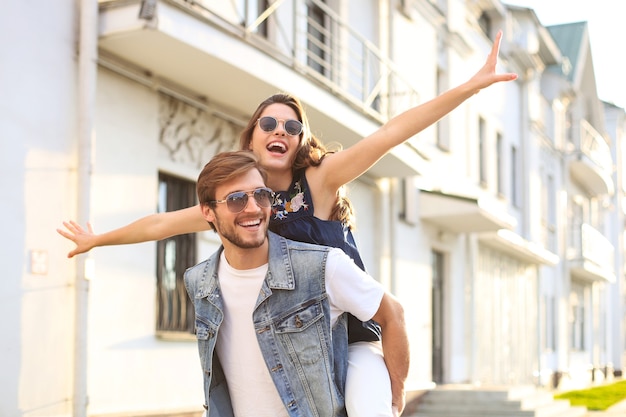 Bel giovane che porta una giovane donna attraente sulle spalle mentre trascorre del tempo insieme all'aperto.