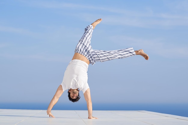 bel giovane che pratica yoga nella moderna terrazza domestica con l'oceano e il tramonto sullo sfondo