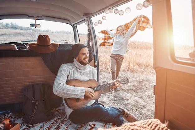 Bel giovane che suona la chitarra per la sua ragazza mentre trascorre del tempo in camper