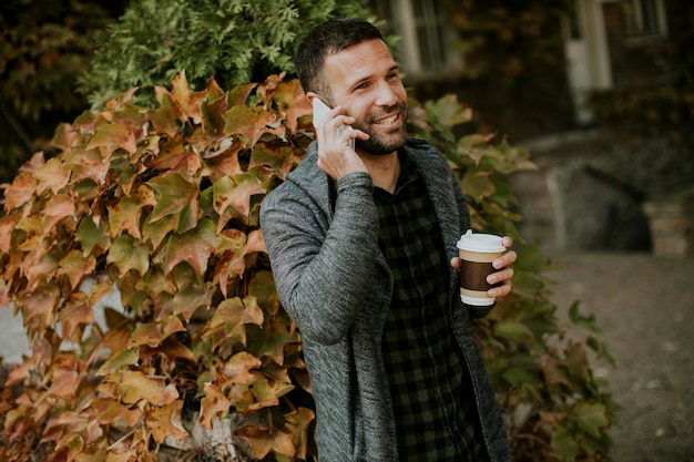 Bel giovane che usa il telefono cellulare e tiene caffè da asporto nel parco