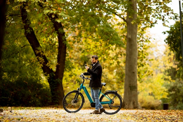 Bel giovane con bicicletta elettrica nel parco autunnale