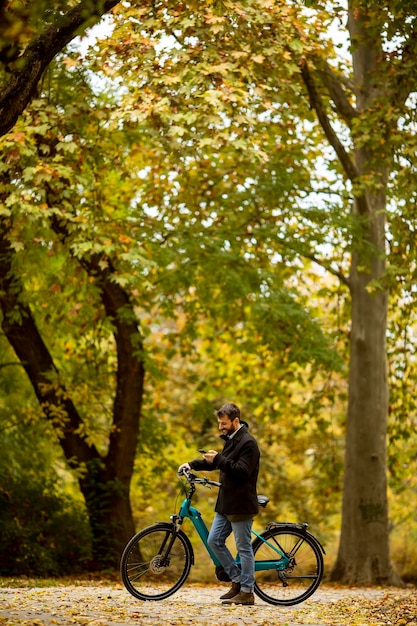 Bel giovane con bicicletta elettrica nel parco autunnale