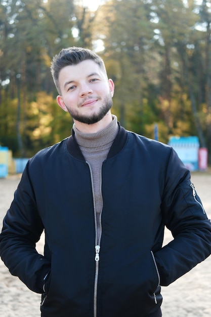 Bel giovane con la barba e una giacca nera in posa sulla spiaggia Vita lenta Godendo delle piccole cose Concetto di Lykke