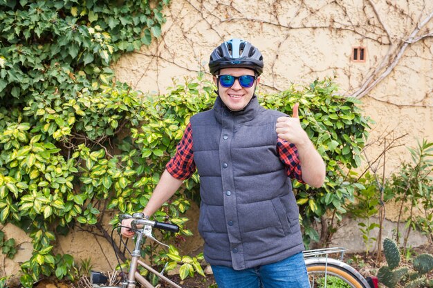 Bel giovane con la bicicletta che mostra i pollici in su nel parco in giornata di sole