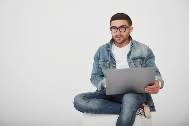 Bel giovane con laptop e controllare il suo orario su sfondo bianco.