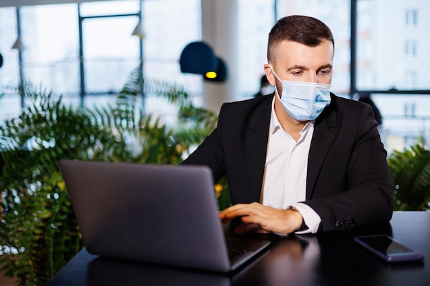 Bel giovane con una maschera che lavora in un bar con un laptop durante la pandemia di coronavirus.