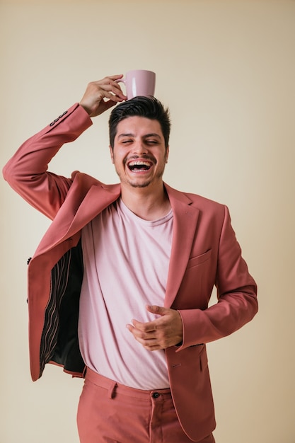 Bel giovane con una tazza rosa in testa vestito con un abito rosa e una camicia