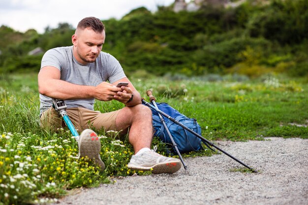 Bel giovane disabile seduto sull'erba mentre usa il suo smartphone