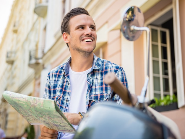 Bel giovane è seduto su uno scooter con una mappa.