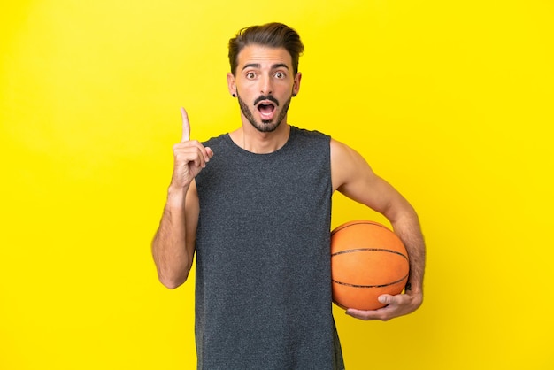 Bel giovane giocatore di basket uomo isolato su sfondo giallo pensando a un'idea che punta il dito verso l'alto