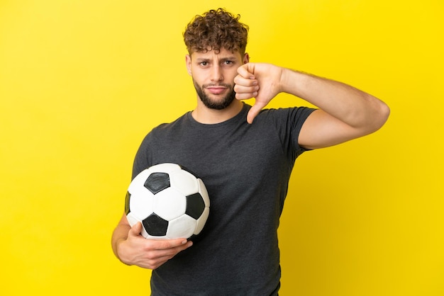 Bel giovane giocatore di football uomo isolato su sfondo giallo che mostra il pollice verso il basso con espressione negativa