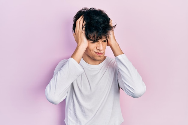 Bel giovane hipster che indossa una camicia bianca casual che soffre di mal di testa disperato e stressato perché dolore ed emicrania. mani sulla testa.