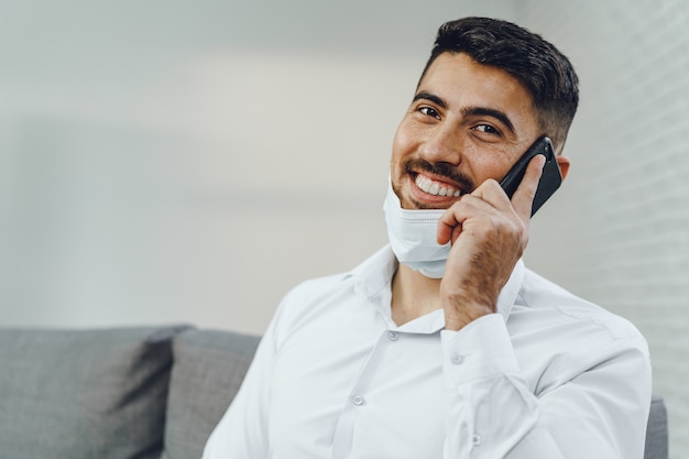 Bel giovane imprenditore con maschera facciale parlando al telefono, ritratto