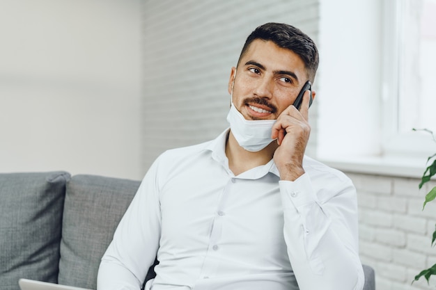 Bel giovane imprenditore con maschera facciale parlando al telefono, ritratto