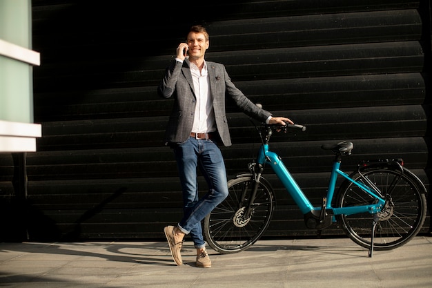 Bel giovane imprenditore in piedi vicino all'ebike e utilizzando il cellulare