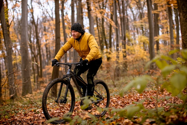 Bel giovane in bicicletta attraverso la foresta autunnale