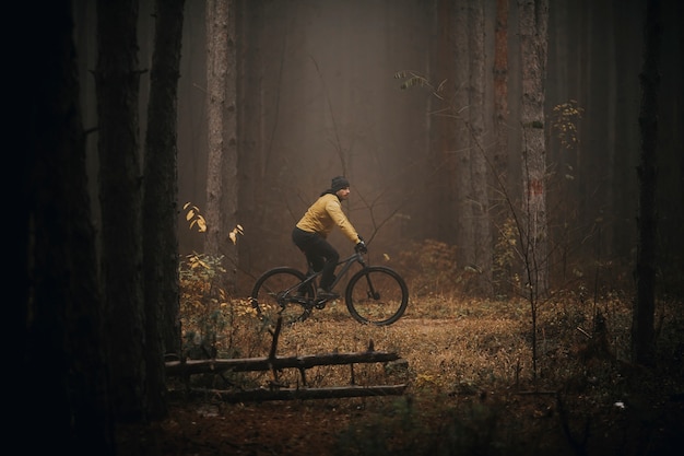 Bel giovane in bicicletta attraverso la foresta di autunno