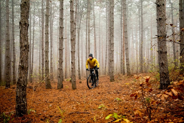 Bel giovane in bicicletta attraverso la foresta di autunno