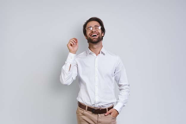 Bel giovane in camicia bianca che sembra felice mentre sta in piedi su uno sfondo grigio