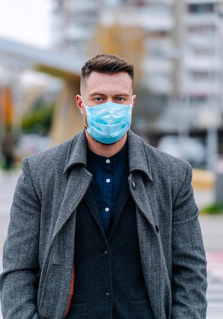Bel giovane in cappotto e tuta per strada con una maschera medica sulla protezione contro le infezioni Virus dell'influenza o coronavirus