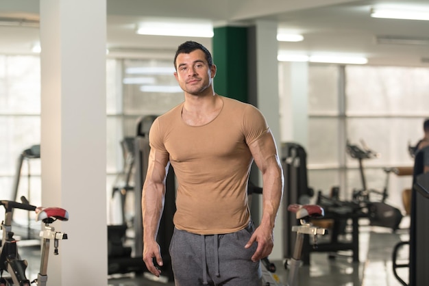 Bel giovane in piedi forte in maglietta marrone e muscoli flettenti Muscoloso atletico culturista modello di fitness in posa dopo gli esercizi