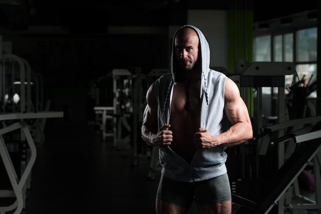 Bel giovane in piedi forte in palestra e flettendo i muscoli Muscoloso atletico culturista modello di fitness in posa dopo gli esercizi