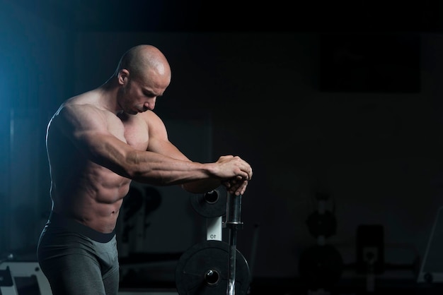 Bel giovane in piedi forte in palestra e flettendo i muscoli Muscoloso atletico culturista modello di fitness in posa dopo gli esercizi