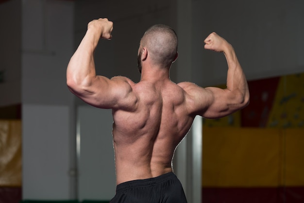 Bel giovane in piedi forte in palestra e flettendo i muscoli Muscoloso atletico culturista modello di fitness in posa dopo gli esercizi