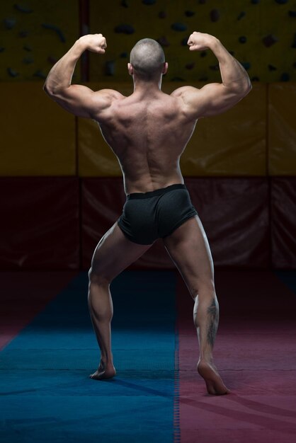 Bel giovane in piedi forte in palestra e flettendo i muscoli Muscoloso atletico culturista modello di fitness in posa dopo gli esercizi
