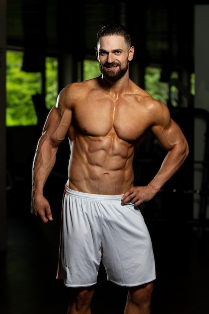 Bel giovane in piedi forte in palestra e flettendo i muscoli Muscoloso atletico culturista modello di fitness in posa dopo gli esercizi