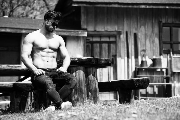 Bel giovane modello si siede forte all'aperto e flette i muscoli Muscoloso bodybuilder atletico uomo che posa un posto per il tuo testo