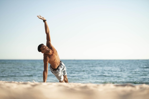 Bel giovane nero in topless danza break dance saltando verticale che gira in posa a testa in giù sulla spiaggia di sabbia