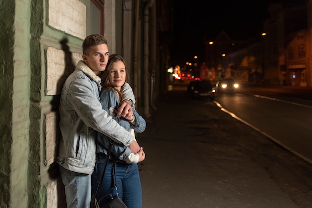 Bel giovane ragazzo abbraccia la sua ragazza sullo sfondo della città di notte. Giovane coppia in un appuntamento romantico serale.