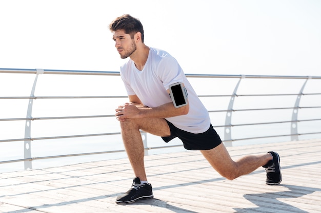 Bel giovane sportivo che allunga le gambe durante l'allenamento sul molo