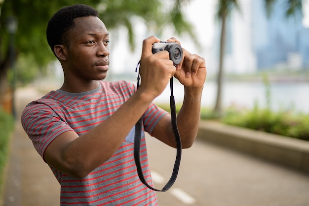 Bel giovane uomo africano a scattare foto con la fotocamera nel parco