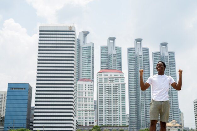 Bel giovane uomo africano con le braccia alzate all'aperto con il paesaggio urbano