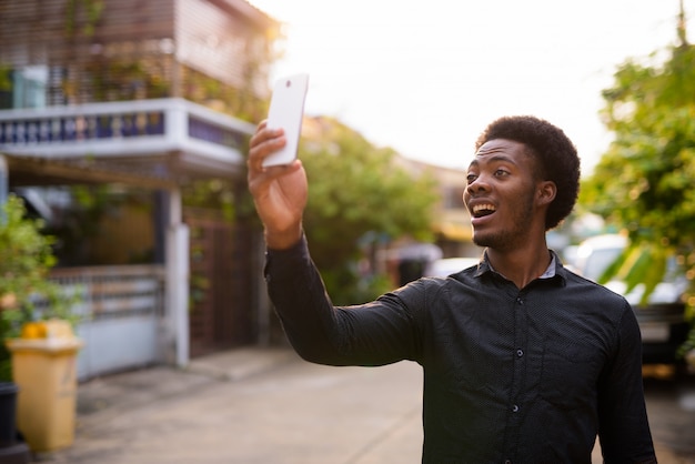 Bel giovane uomo africano utilizzando il telefono cellulare all'aperto