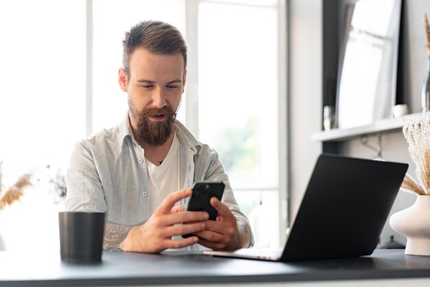 Bel giovane uomo barbuto che trascorre del tempo a casa con il telefono in mano