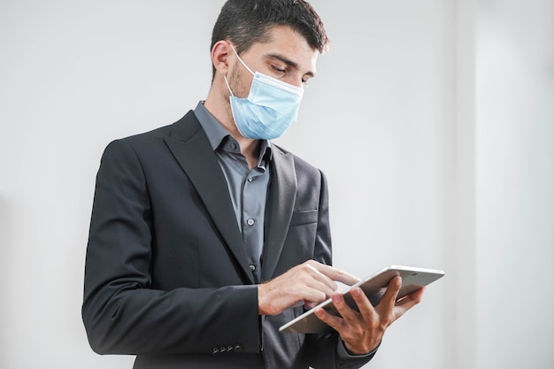 Bel giovane uomo d'affari che indossa una maschera protettiva che lavora con un tablet su uno sfondo bianco