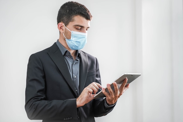 Bel giovane uomo d'affari che indossa una maschera protettiva che lavora con un tablet su uno sfondo bianco